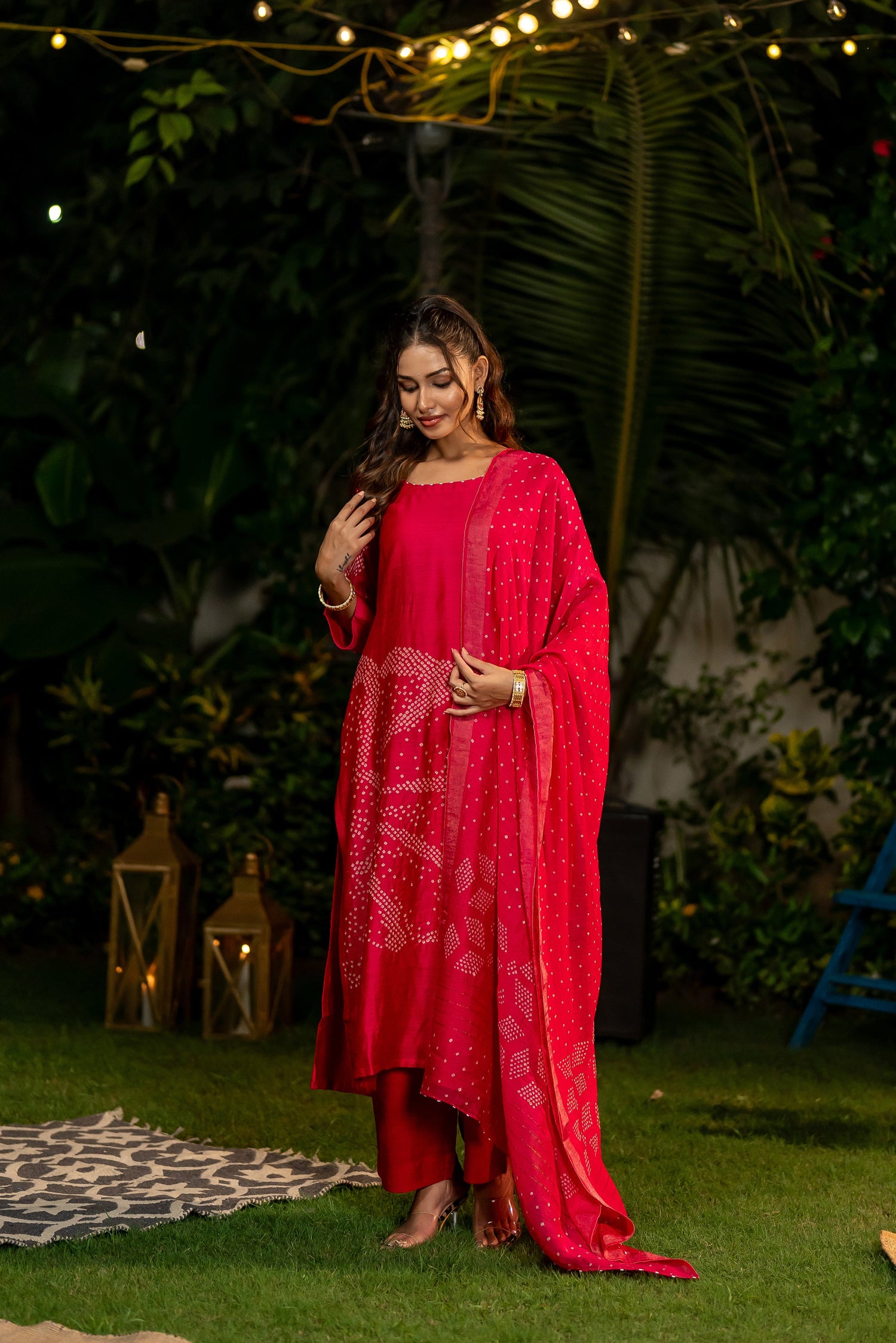 Woman in a pink traditional outfit standing outdoors with string lights and lanterns in the background.